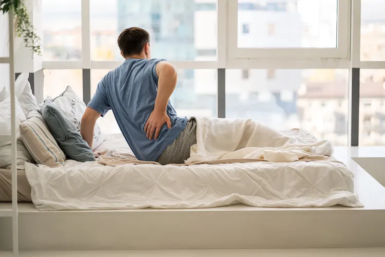 Man holding his lower back while getting out of bed